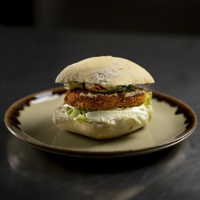 Panino plant-based con cotoletta croccante, carpaccio di verdure e salsa tartara su tagliere