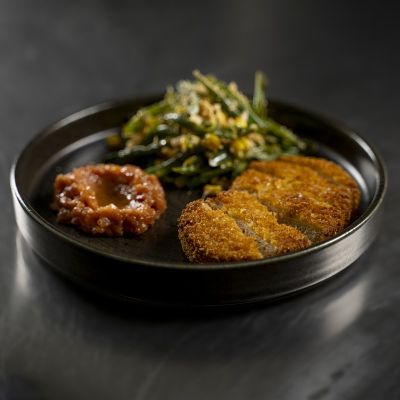 Cotoletta vegetale tagliata con salsa alle pesche e insalata di fagiolini e mais guarnita con arachidi.