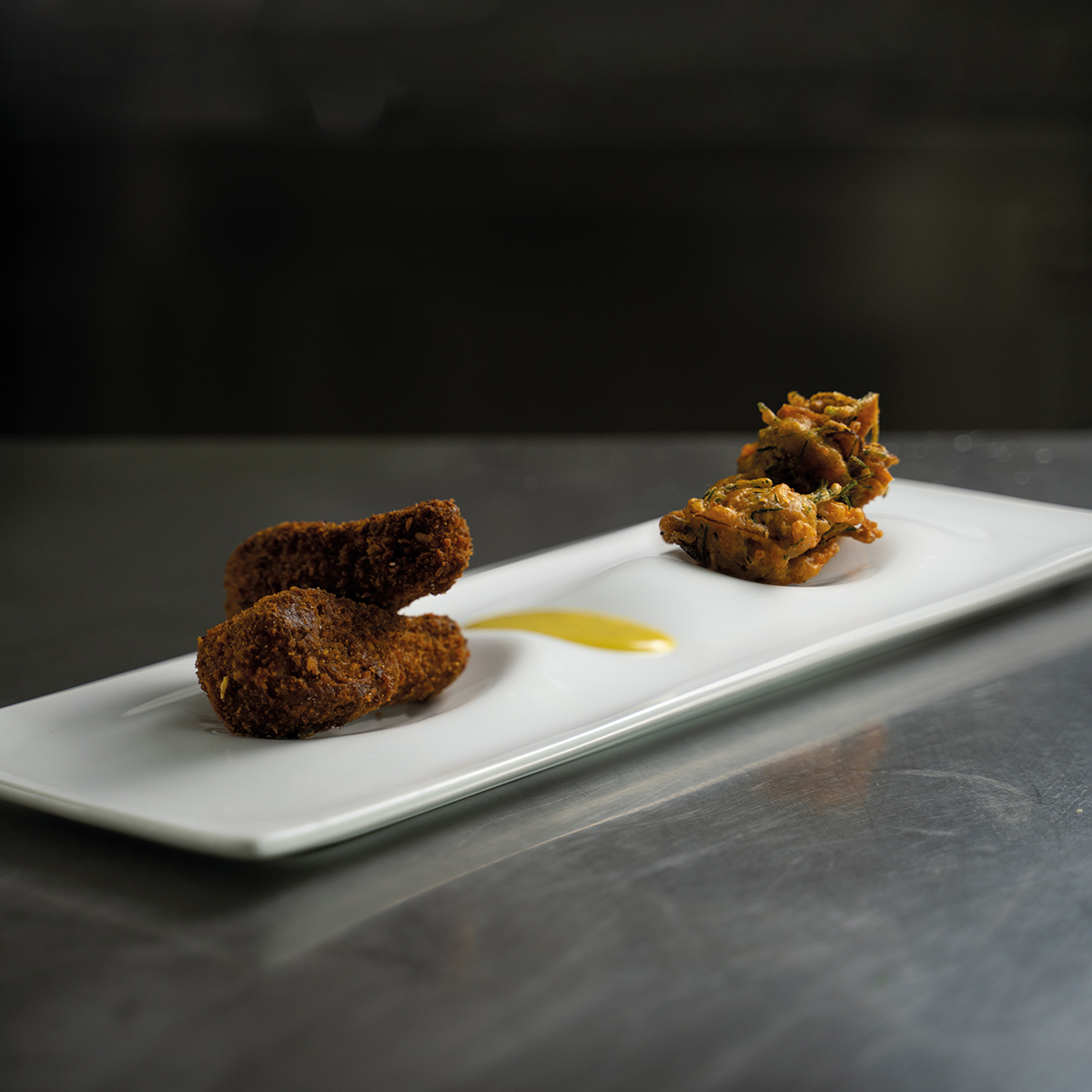 Cosciotti vegani fritti serviti con pakora croccanti e salsa cremosa al curry e cocco, su piatto bianco.