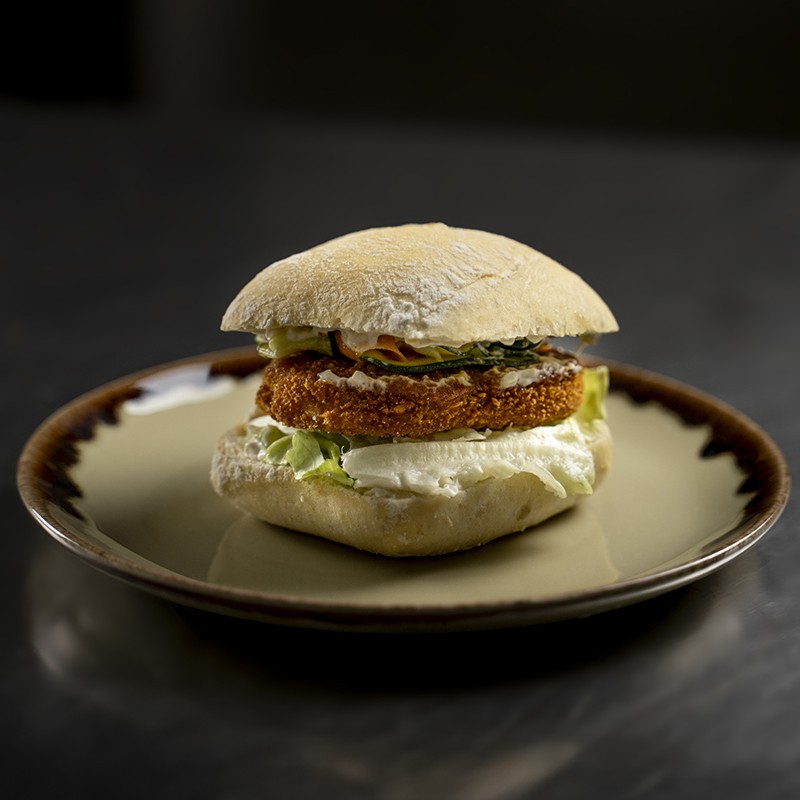 Panino plant-based con cotoletta croccante, carpaccio di verdure e salsa tartara su tagliere